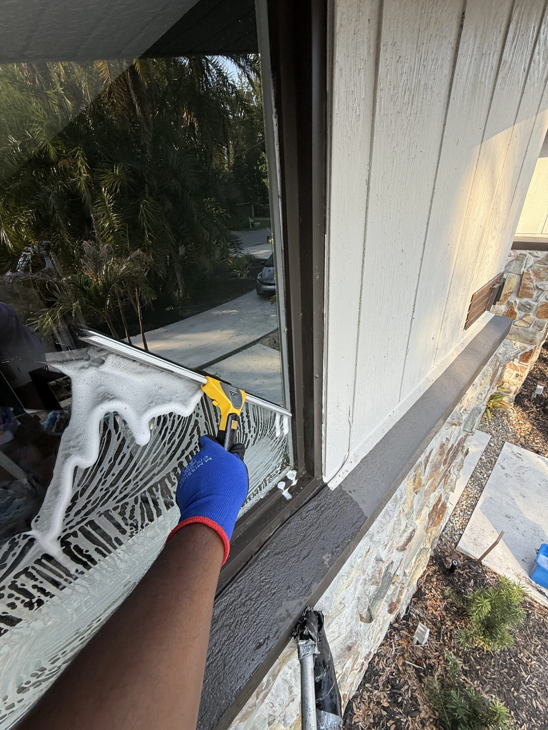 Technician washing a soapy window with a strip washer on a Tampa Bay home