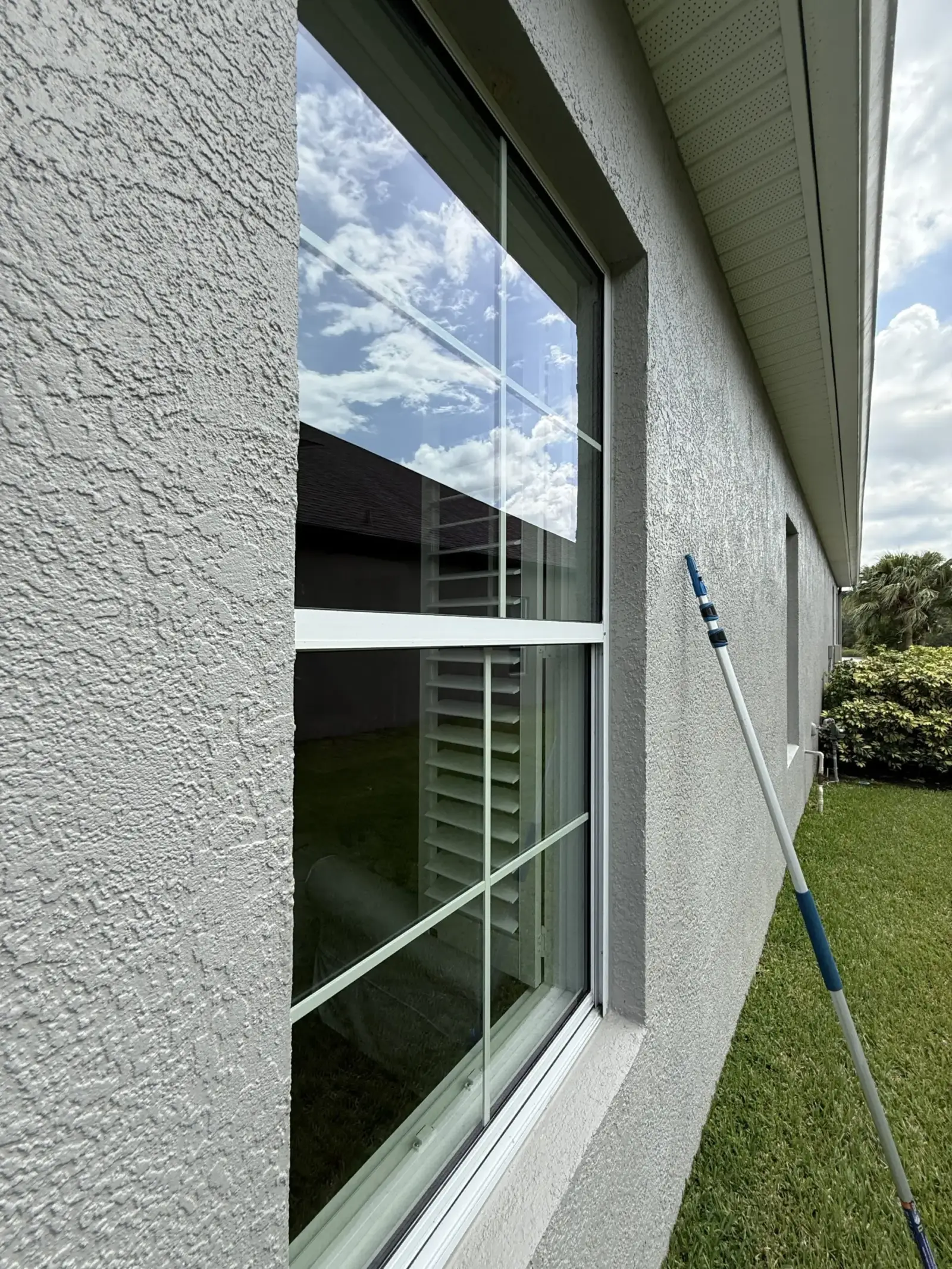 Clean window on a stucco home after window cleaning, with a water-fed pole beside it