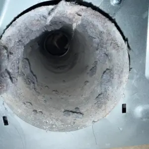 Lint and dust caked inside the opening of a dryer duct, before cleaning