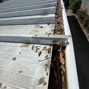 Gutter packed with leaves and debris along a metal roof before gutter cleaning