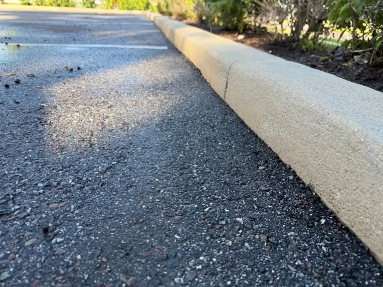 A parking lot curb after pressure washing, with the concrete clean again