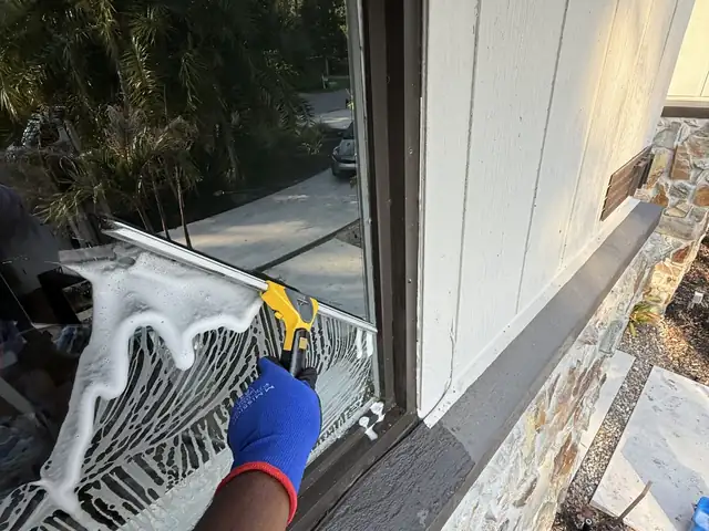 Technician washing a soapy window with a strip washer on a Tampa Bay home