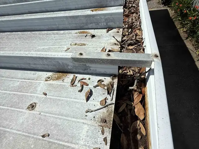 Gutter packed with leaves and debris along a metal roof before gutter cleaning